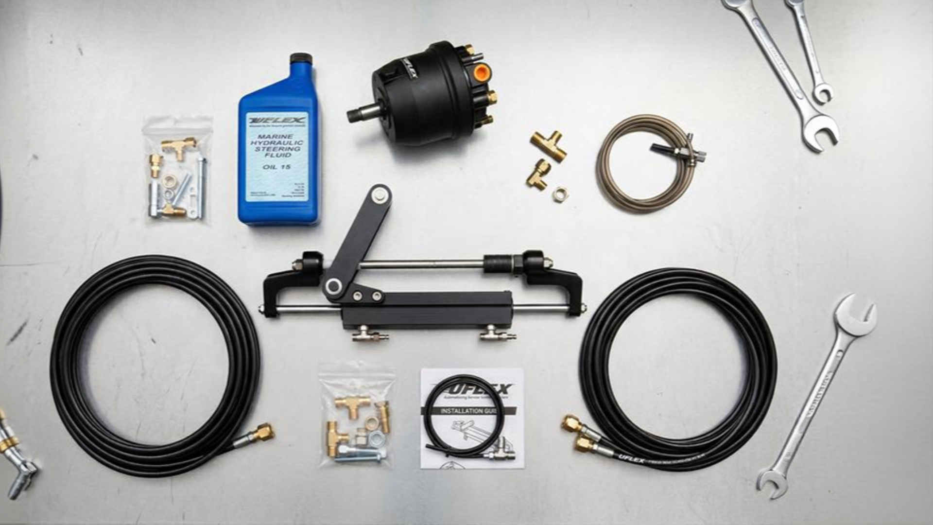 hydraulic steering kit component laid out for installation;includes black hydraulic cylinder, helm pump, hoses,steering fluid, brass fittings, & installation guide.