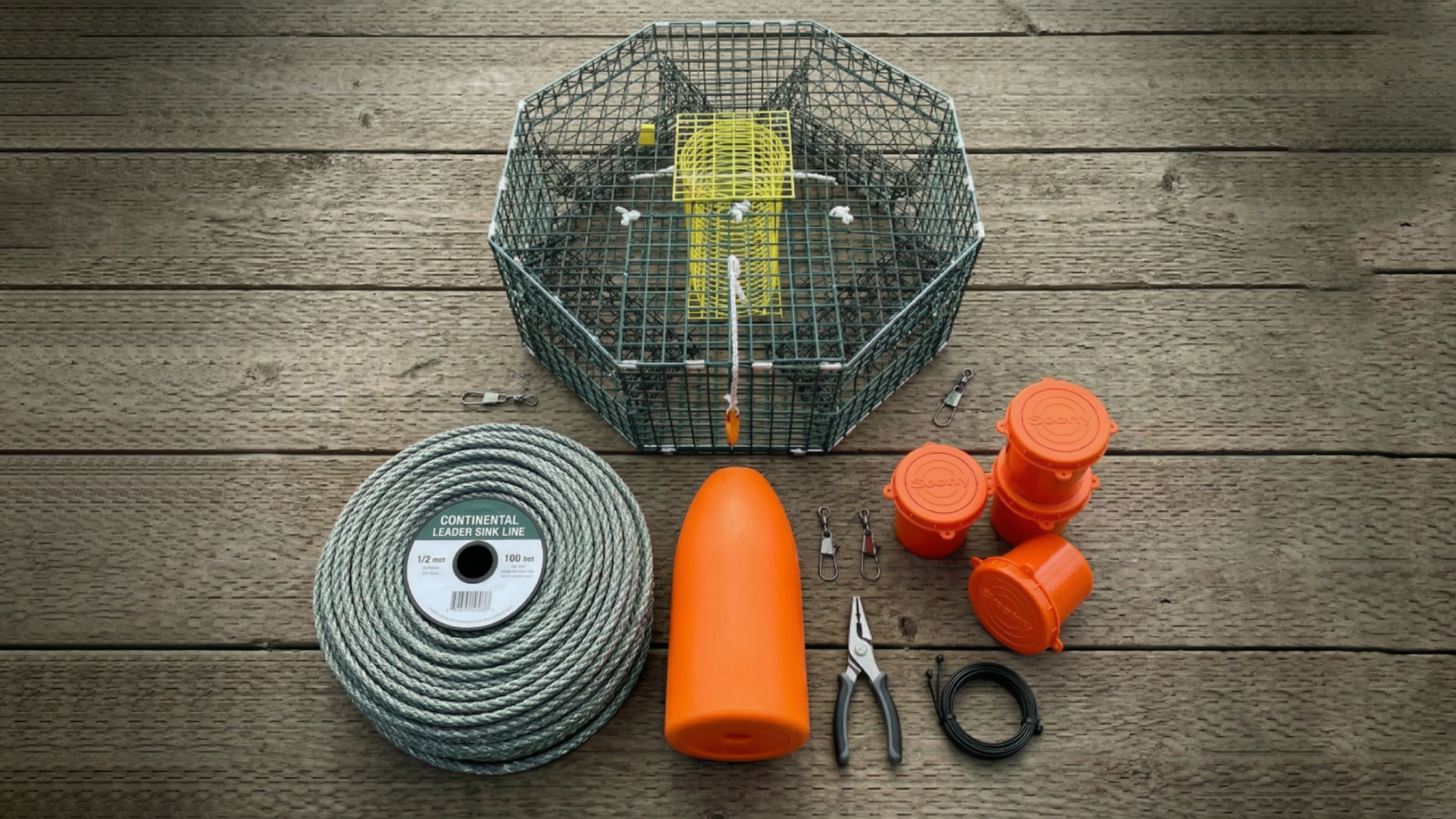 Complete crab fishing gear, featuring an octagonal crab trap, a Continental Leader Sink Line, a large orange buoy, bait jars, plier, and rigging clips.