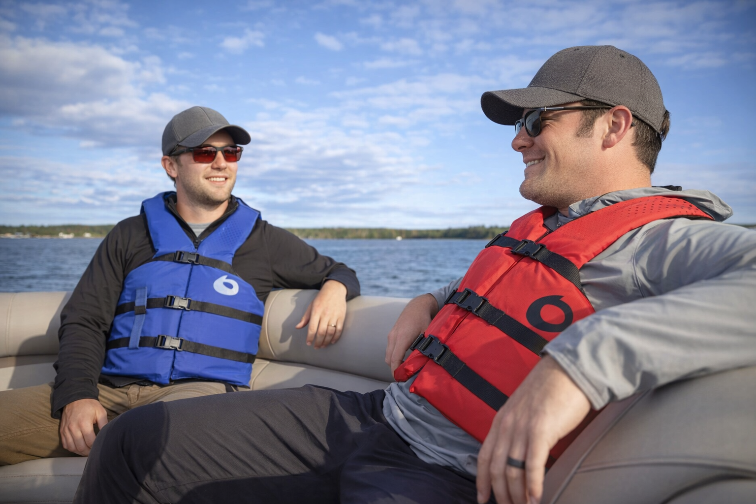 Two men wearing red and blue Type III life jackets while relaxing on a boat, demonstrating recreational boating safety
