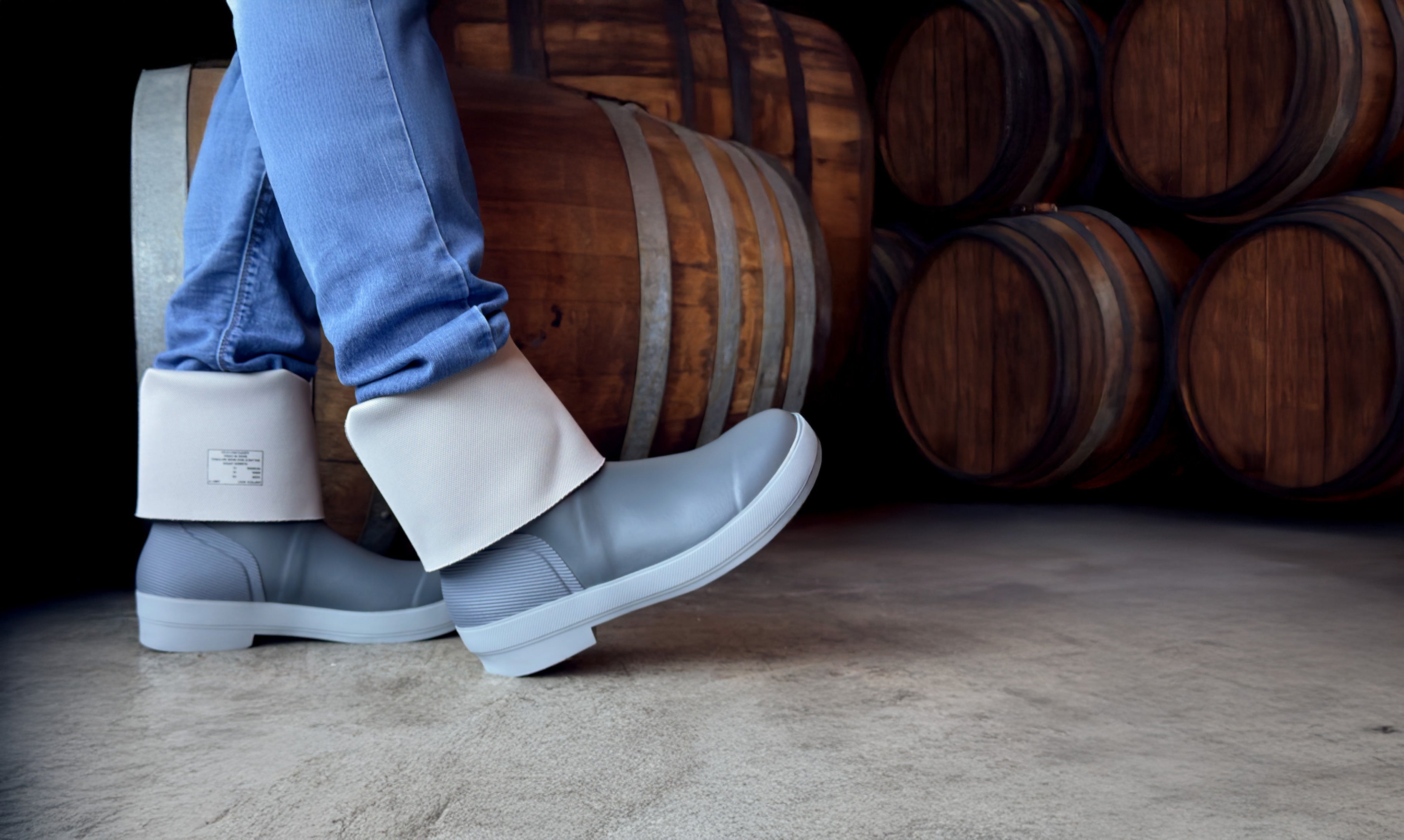 Person wearing blue rubber boots with white cuffs in front of wooden barrels.